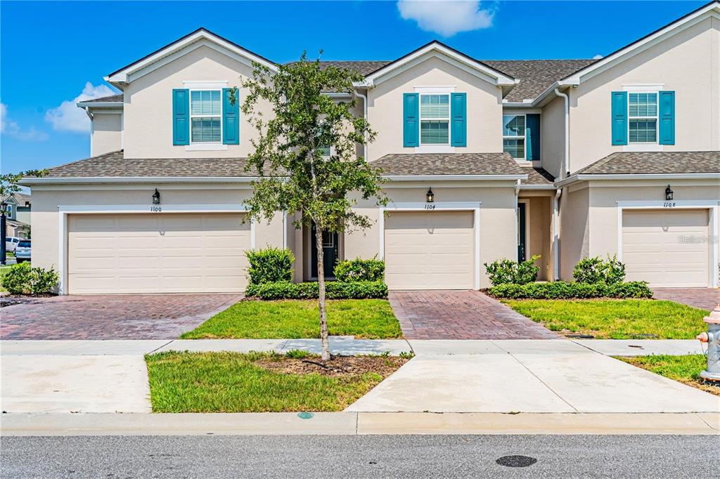 A row of three beige townhouses with attached garages and blue window shutters — 1104 LAKESHORE BREEZE PLACE, KISSIMMEE, FL