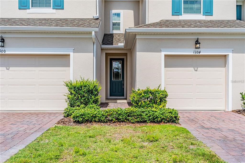 The exterior view shows a two-story townhouse with two beige garage doors and a central entrance — 1104 LAKESHORE BREEZE PLACE, KISSIMMEE, FL