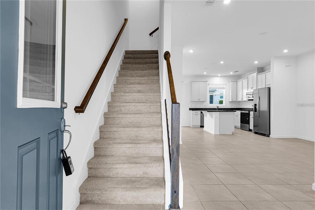 A carpeted staircase leads to an upper level next to an open-concept kitchen and living area — 1104 LAKESHORE BREEZE PLACE, KISSIMMEE, FL