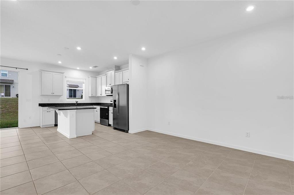 A kitchen with white cabinets, dark countertops, and an island opens to a tiled area — 1104 LAKESHORE BREEZE PLACE, KISSIMMEE, FL