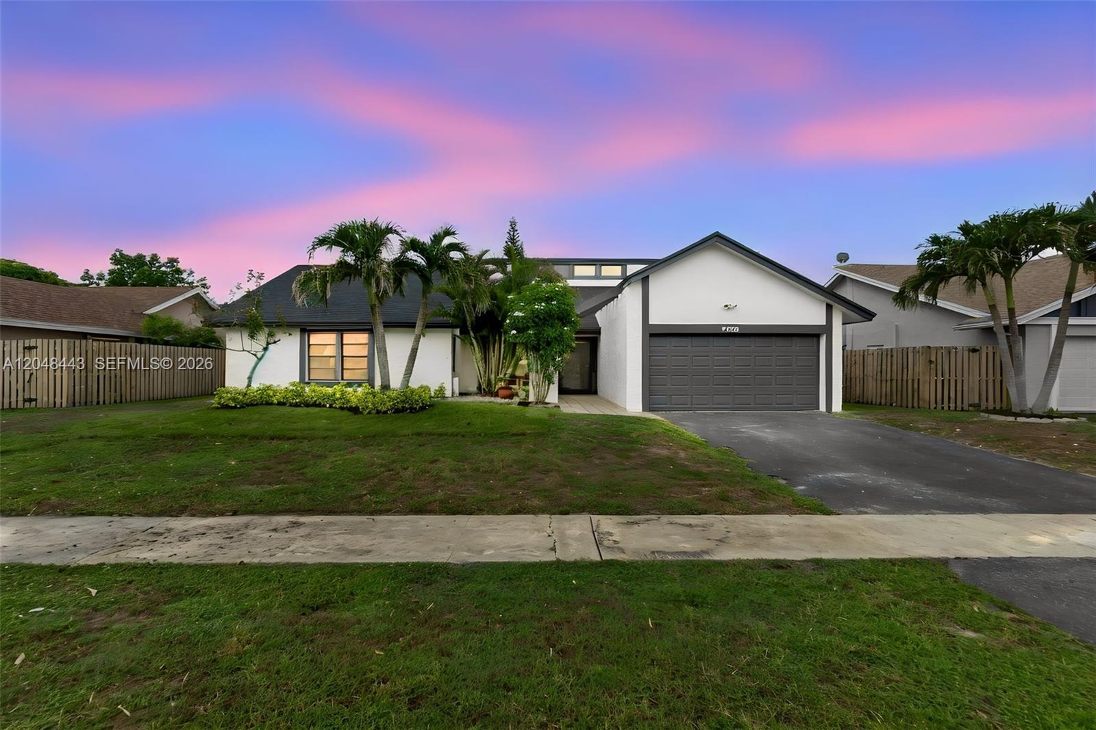 A single-story house with a white exterior, dark garage door, and palm trees at dusk — 7428 NW 49th Ct, Lauderhill FL 33319, LAUDERHILL, FL
