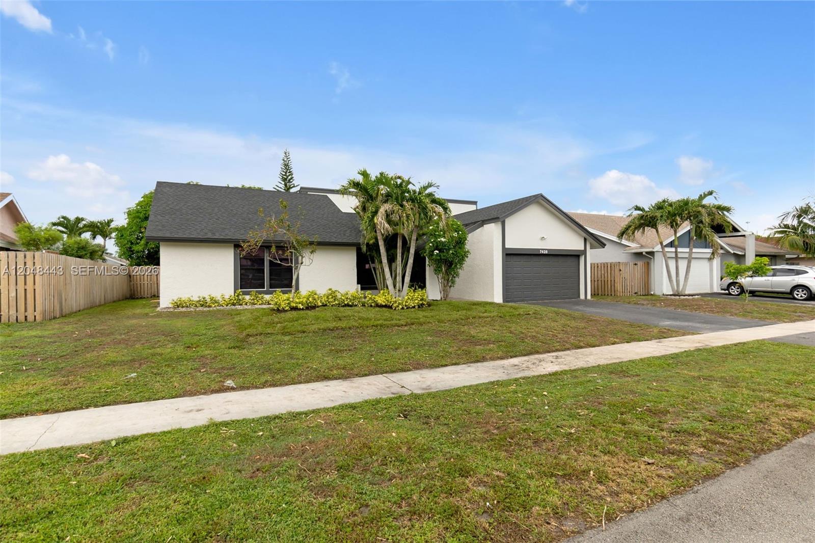 A single-story house with a white exterior, dark roof, attached garage, and palm trees — 7428 NW 49th Ct, Lauderhill FL 33319, LAUDERHILL, FL
