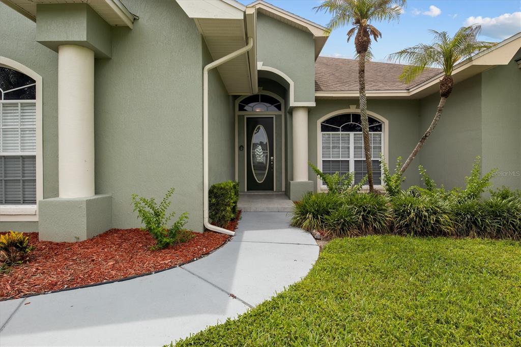 A light green house exterior features a front entrance with a walkway and palm trees — 5446 HIGHLANDS VISTA CIRCLE, LAKELAND, FL