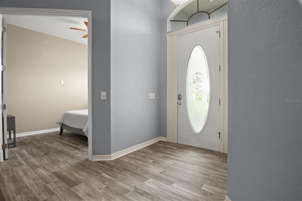 An entryway with wood-look tile flooring leads to a front door and a bedroom doorway — 5446 HIGHLANDS VISTA CIRCLE, LAKELAND, FL