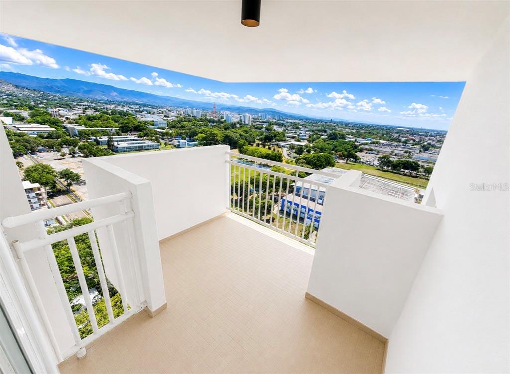 A high-rise balcony with white railings overlooks a city landscape with trees and mountains — 2325 UNIVERDIDAD STREET UNIT 2302, PONCE, PR