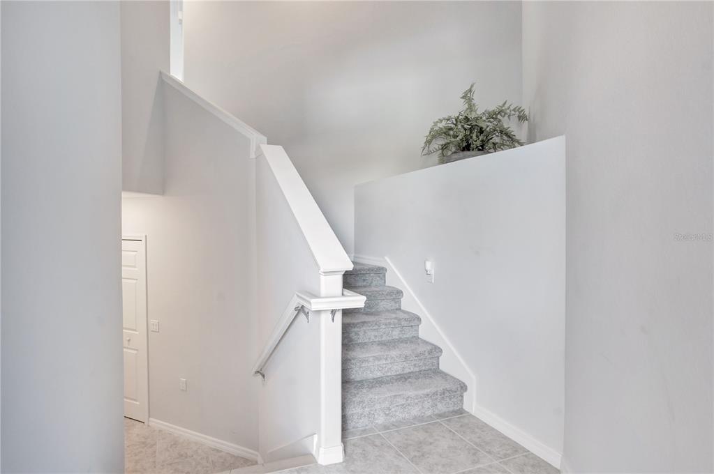 A carpeted staircase with a white railing leads upward in a room with tiled floors — 415 WINDING BROOK LANE UNIT 102, BRADENTON, FL