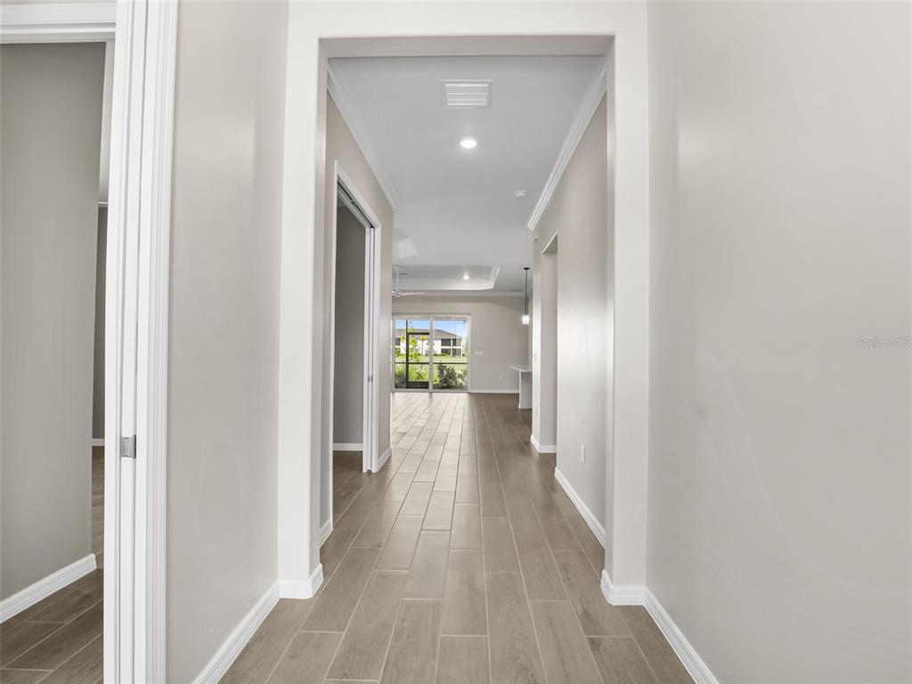 A hallway with light-colored tile flooring leads toward an open living area with sliding doors — 15904 SUGAR HILL DRIVE, PUNTA GORDA, FL