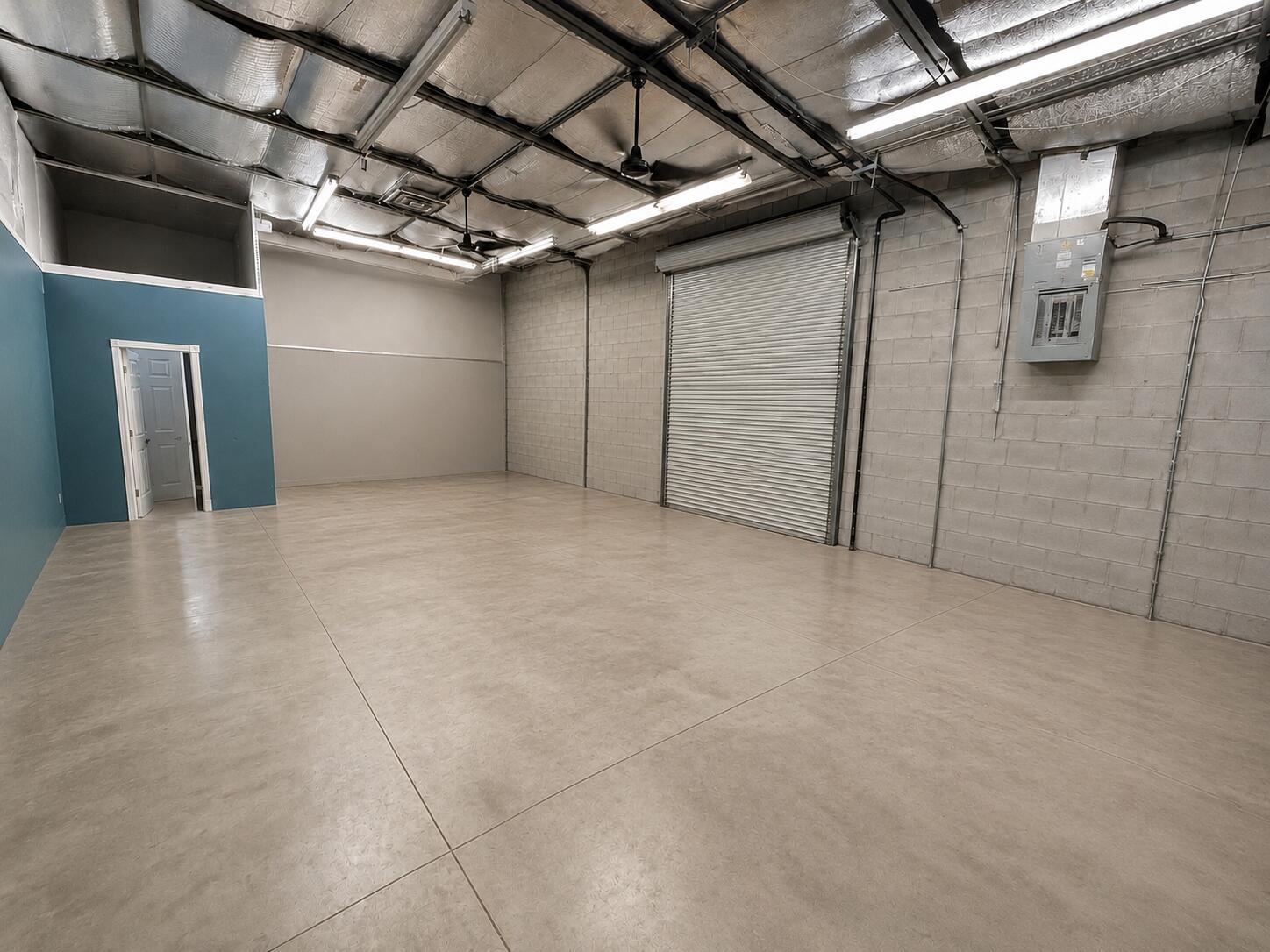 An empty warehouse space with concrete floors, block walls, a roll-up door, and exposed ceiling — 2646 SE Willoughby Boulevard, Stuart FL 34994, STUART, FL