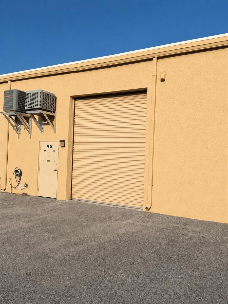 The exterior of a tan commercial building features a roll-up door and a side entrance — 2646 SE Willoughby Boulevard, Stuart FL 34994, STUART, FL
