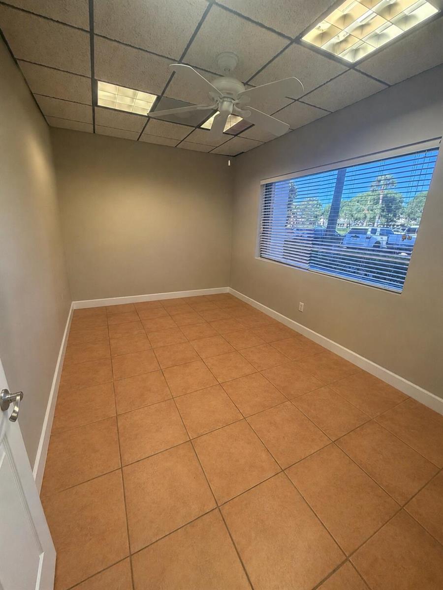 An empty office with beige walls, tan tile flooring, a ceiling fan, and a large window — 2646 SE Willoughby Boulevard, Stuart FL 34994, STUART, FL