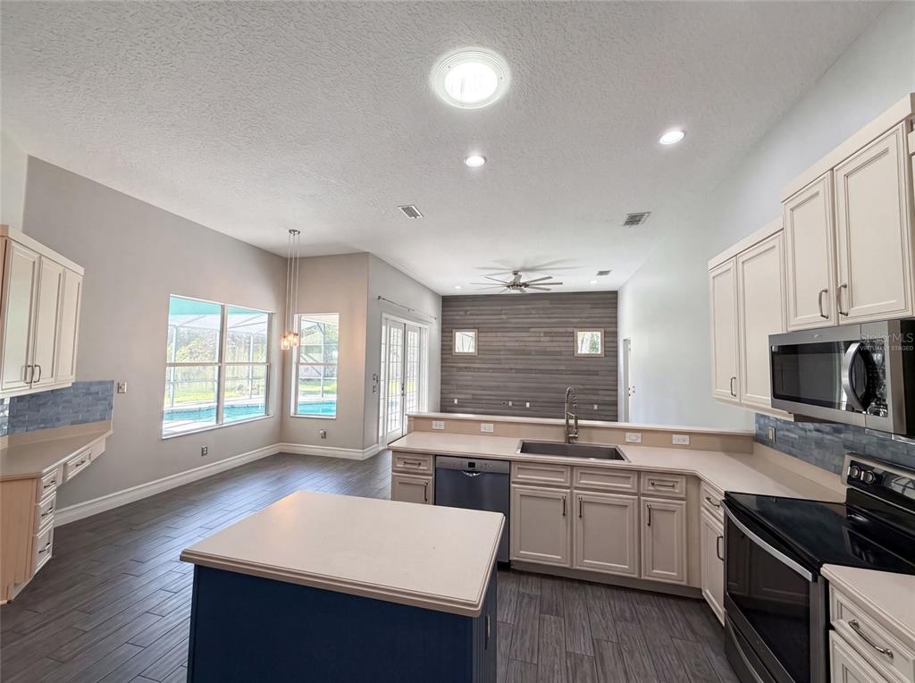 A kitchen with an island, light-colored cabinets, and a wood-paneled accent wall overlooking a pool — 3100 CONRAD COURT, KISSIMMEE, FL