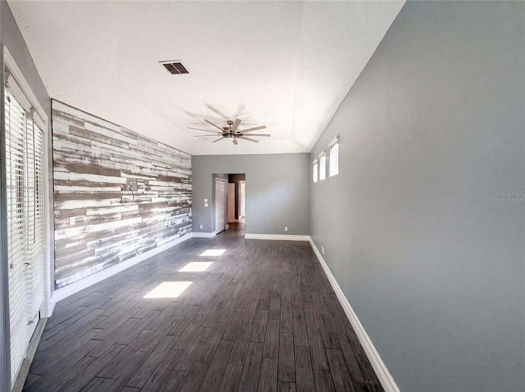 An empty room features gray walls, wood-look tile flooring, and a rustic wood-plank accent wall — 3100 CONRAD COURT, KISSIMMEE, FL