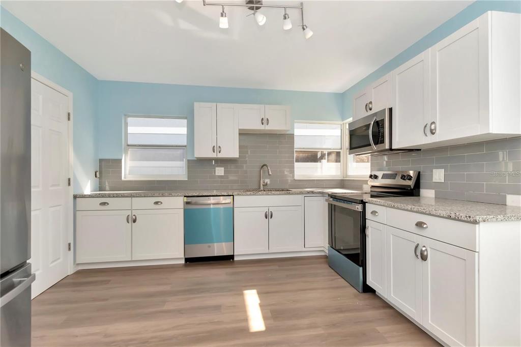 A kitchen with white cabinets, granite countertops, gray subway tile backsplash, and stainless steel appliances — 4512 26TH AVENUE S, TAMPA, FL