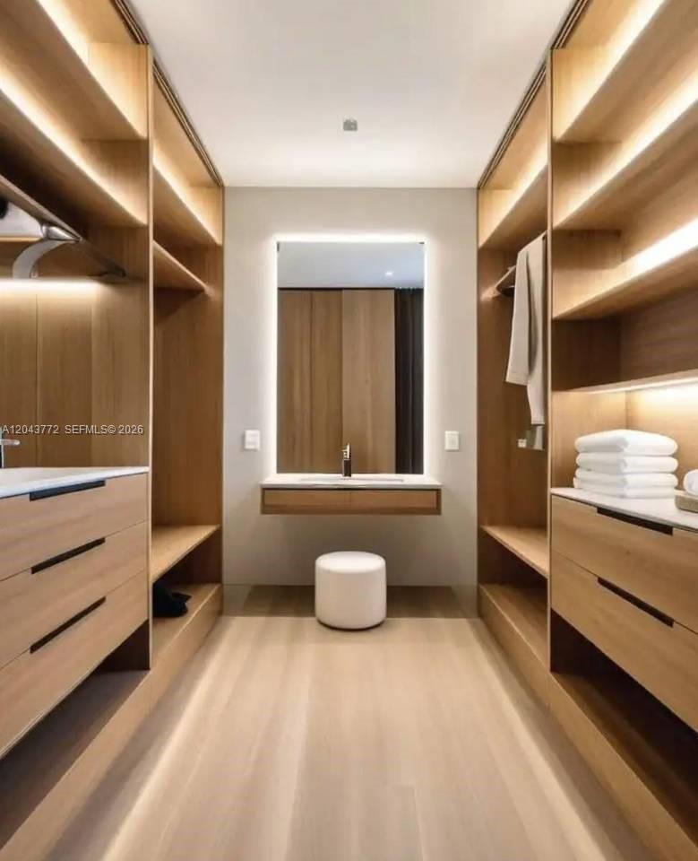 A modern walk-in closet featuring light wood cabinetry, open shelving, and a central vanity mirror — 0 villa banyu, FL