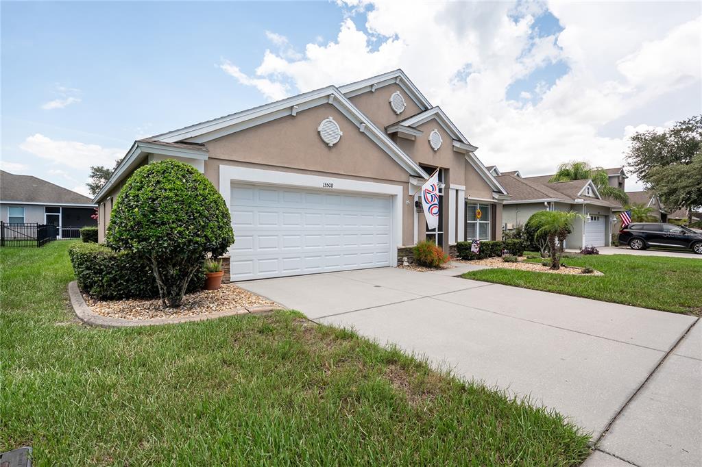 A single-story house with a white garage door, tan stucco exterior, and a landscaped yard — 13508 MEADOW GOLF AVENUE, HUDSON, FL