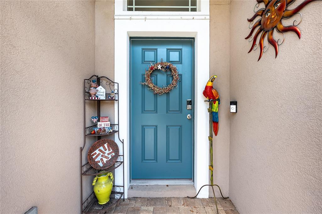 A teal front door with a wreath stands between a metal shelf and a parrot statue — 13508 MEADOW GOLF AVENUE, HUDSON, FL