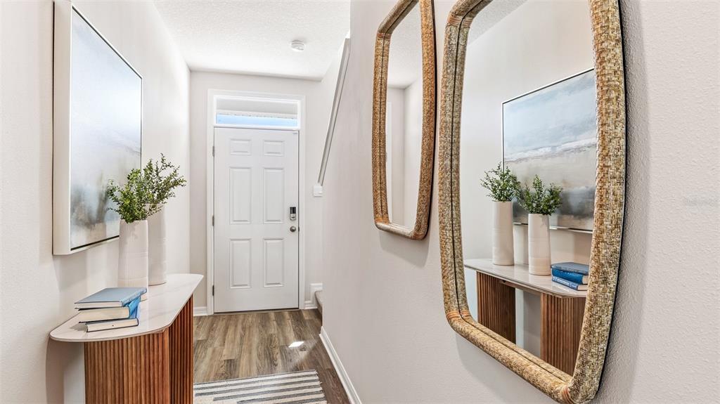 A bright entryway features a white door, wood-look flooring, a console table, and wall mirrors — 4131 MILLER POINTE COURT, BRADENTON, FL