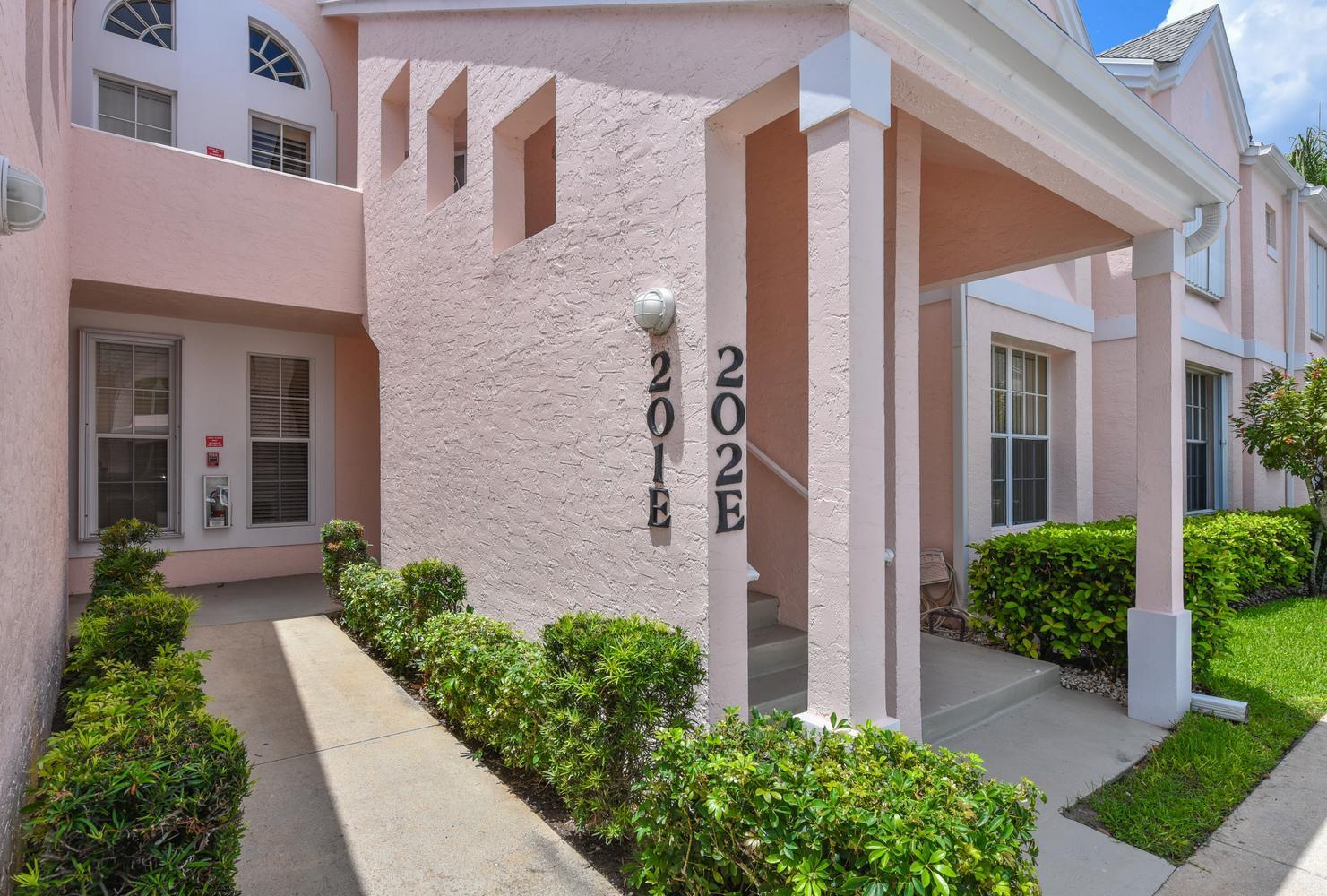 The exterior of a pink stucco building features a walkway, landscaping, and unit numbers — 201 Muirfield Court # 201e, Jupiter FL 33458, JUPITER, FL