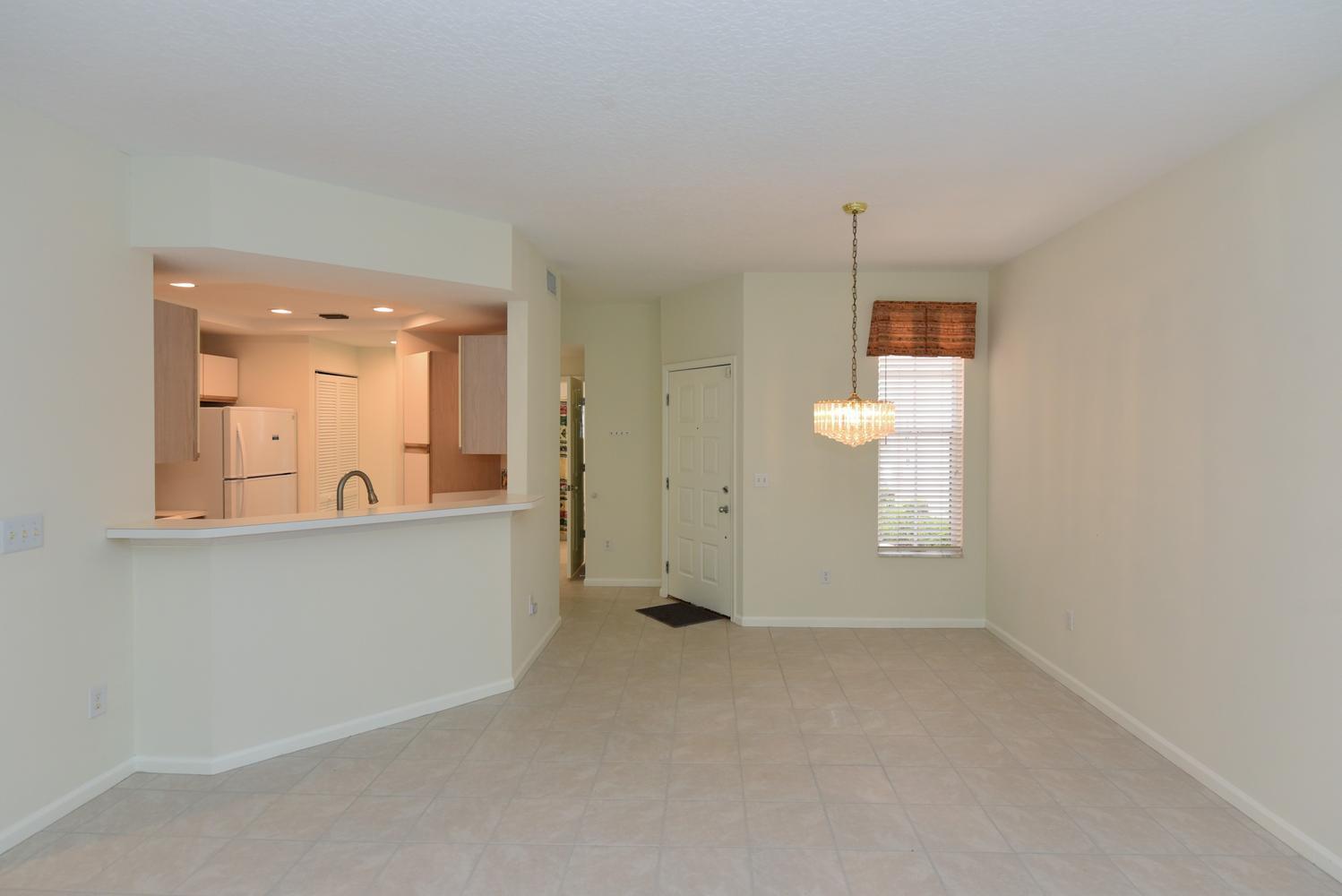 An open-concept dining area with tile flooring, a crystal chandelier, and a kitchen pass-through window — 201 Muirfield Court # 201e, Jupiter FL 33458, JUPITER, FL