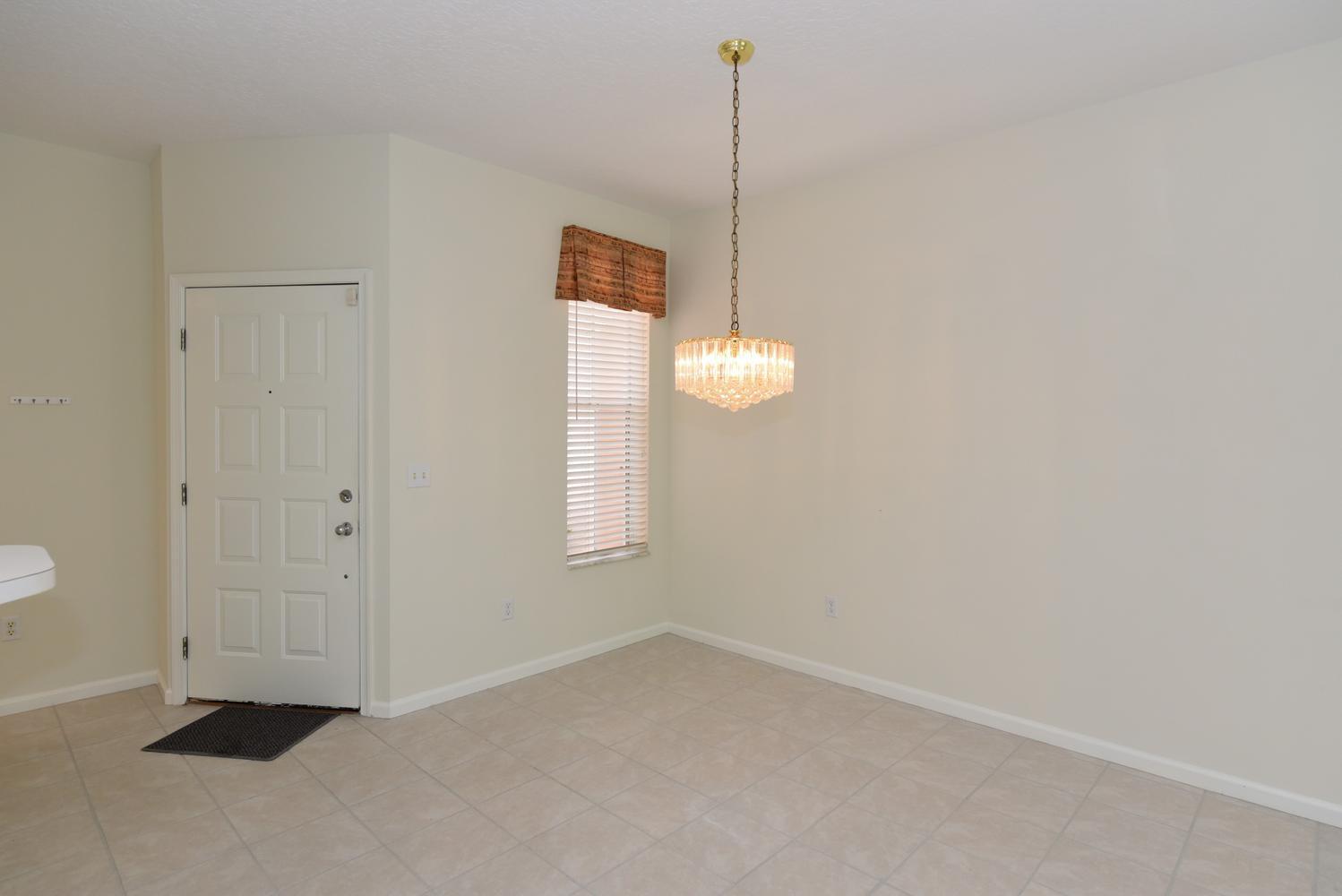 An empty dining area with tile flooring, a crystal chandelier, and a white entry door — 201 Muirfield Court # 201e, Jupiter FL 33458, JUPITER, FL