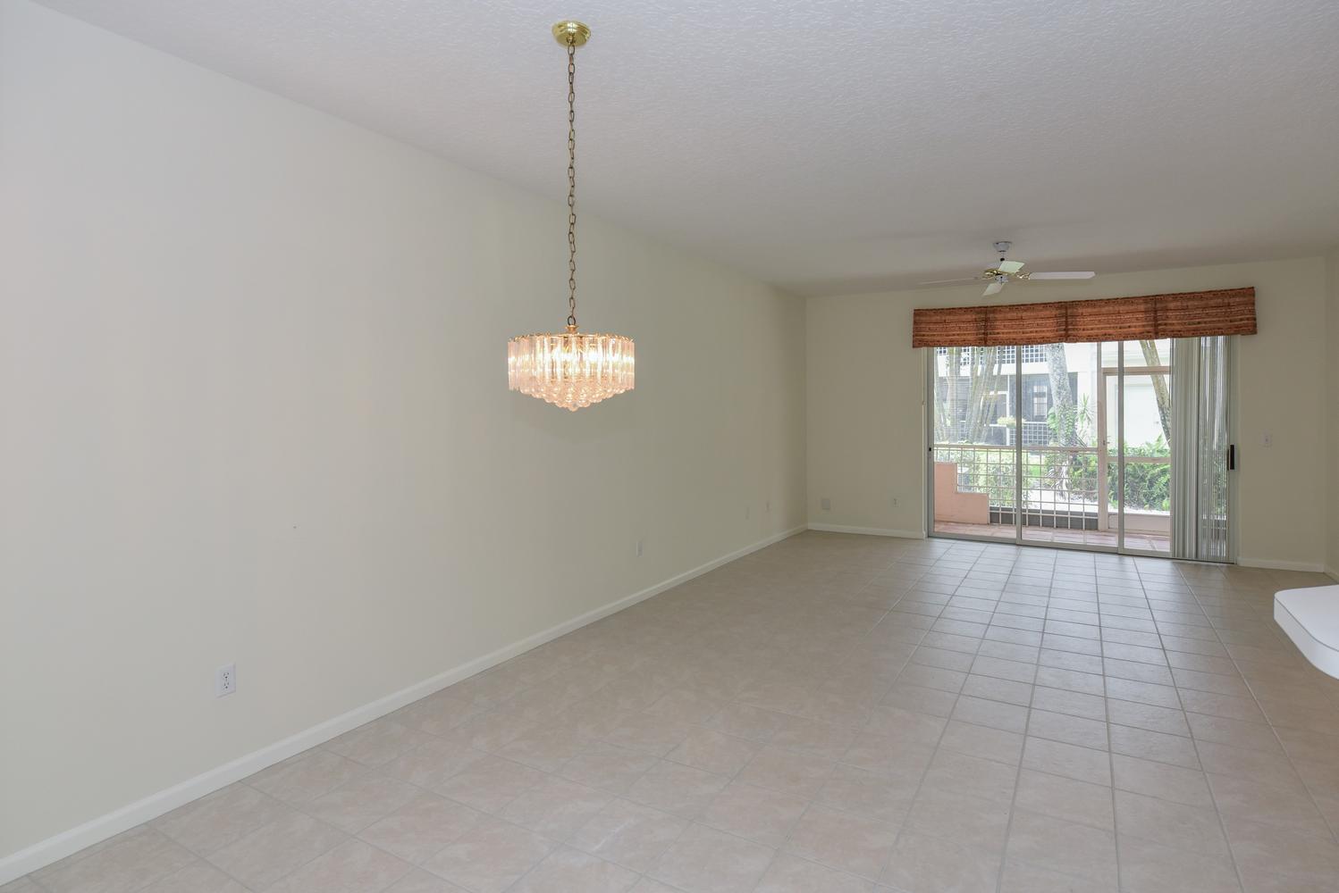 An empty room with beige tile flooring, a crystal chandelier, and sliding glass balcony doors — 201 Muirfield Court # 201e, Jupiter FL 33458, JUPITER, FL