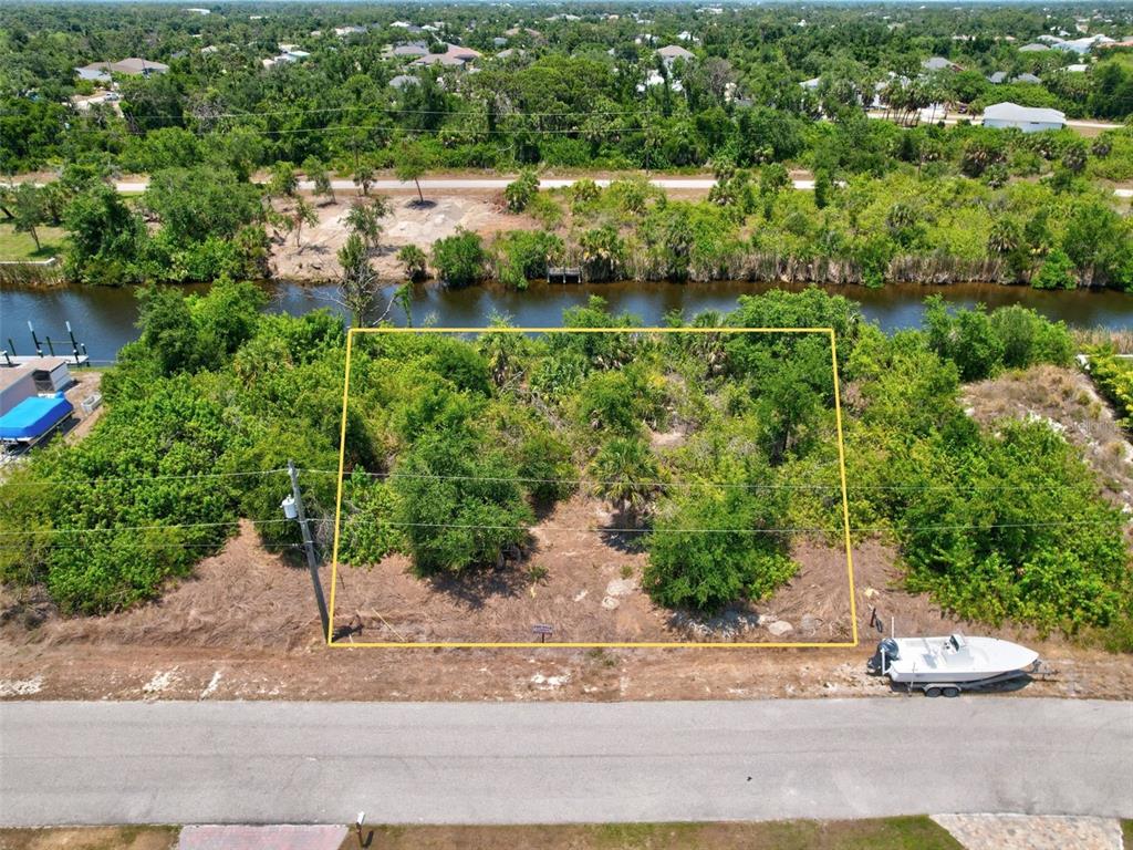 An aerial view shows a vacant, wooded waterfront lot outlined in yellow along a road — 10080 COCOA BEACH STREET, PORT CHARLOTTE, FL