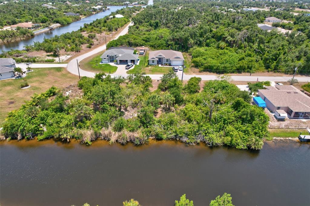 An aerial view shows two houses near a road and a large, wooded waterfront lot — 10080 COCOA BEACH STREET, PORT CHARLOTTE, FL