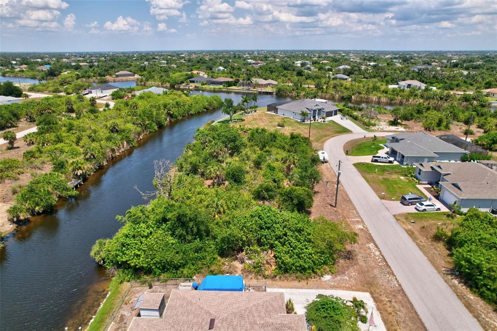 An aerial view shows a residential neighborhood with houses, a winding canal, and lush vegetation — 10080 COCOA BEACH STREET, PORT CHARLOTTE, FL
