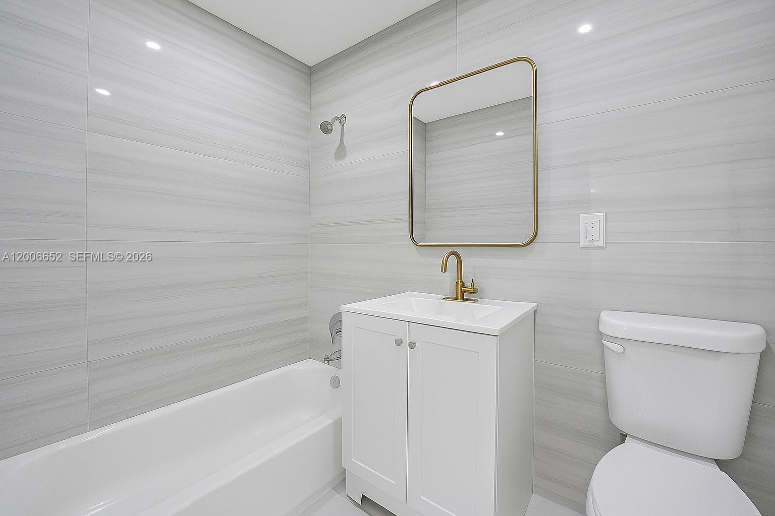 A bathroom features a white vanity, a gold-framed mirror, and gray horizontal-tiled walls — 105 NW 14th Way # 0, Dania Beach FL 33004, DANIA BEACH, FL