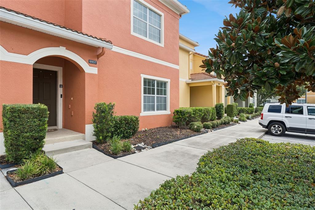An exterior view of a two-story orange stucco townhouse with a front entrance and landscaping — 8957 CAT PALM ROAD, KISSIMMEE, FL