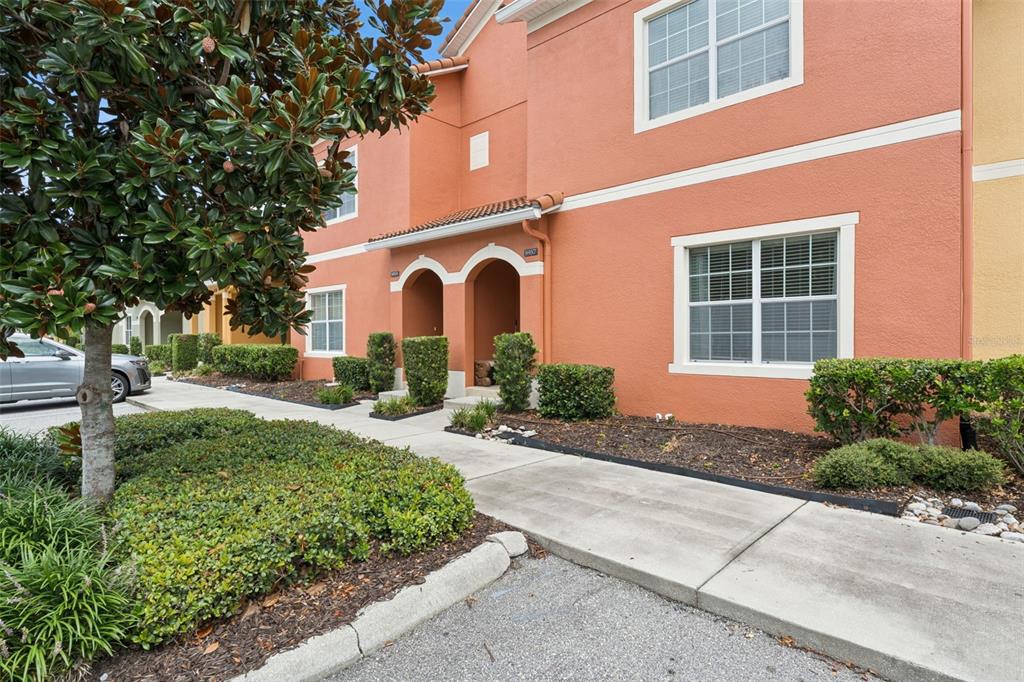 An exterior view of a two-story orange stucco townhouse with a covered entryway and landscaping — 8957 CAT PALM ROAD, KISSIMMEE, FL