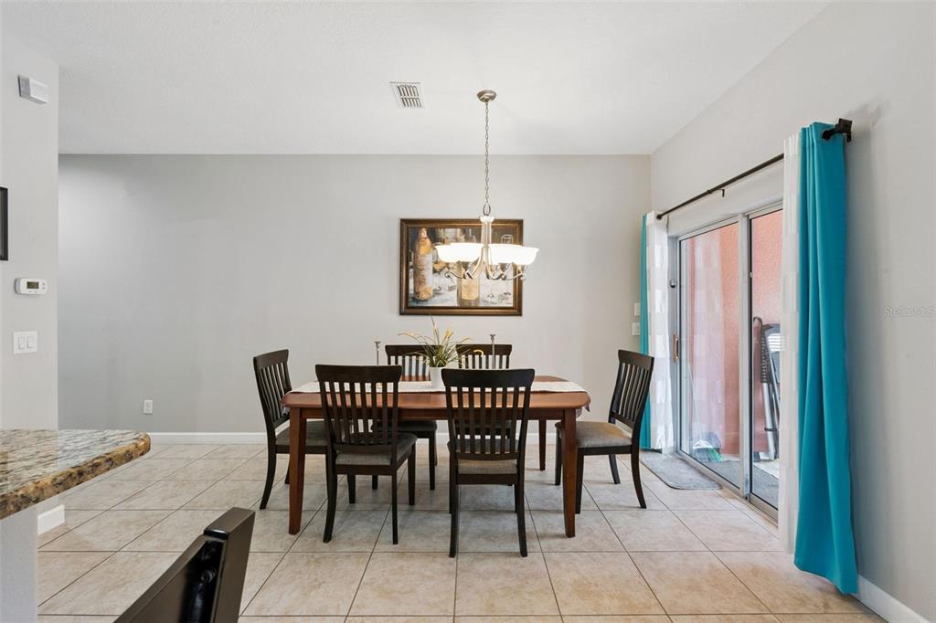 A dining room features a wooden table with six chairs, a chandelier, and sliding glass doors — 8957 CAT PALM ROAD, KISSIMMEE, FL