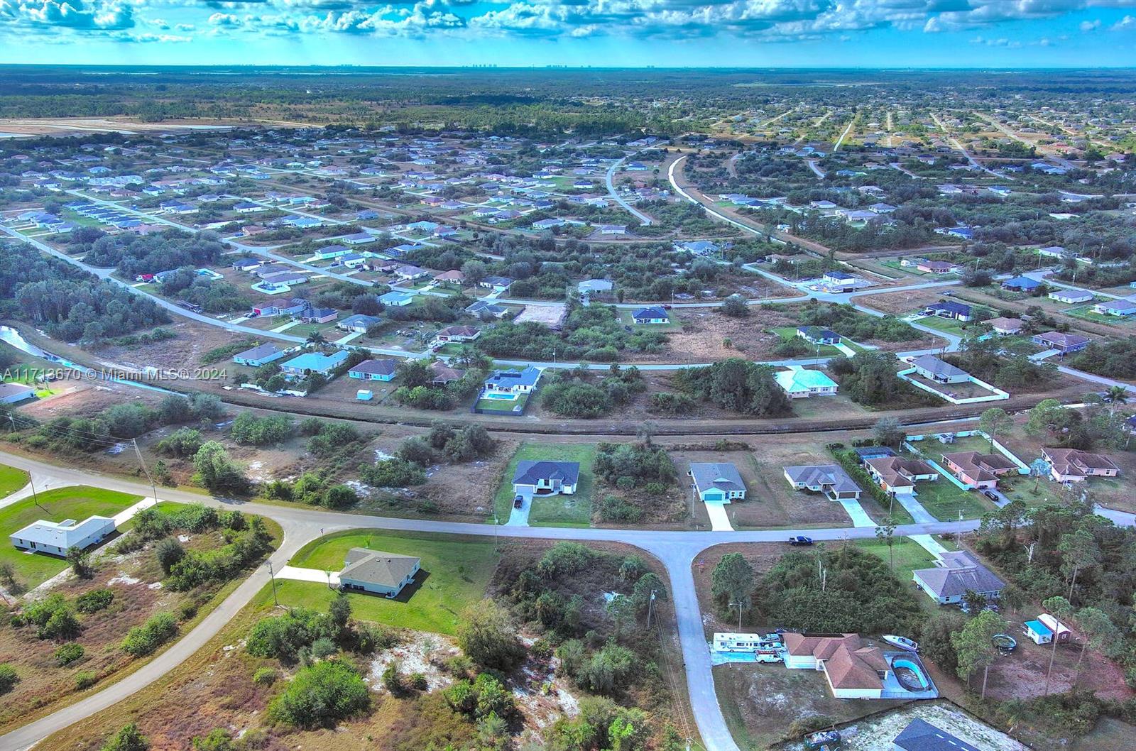 An aerial view shows a residential neighborhood with scattered houses, dirt roads, and surrounding vegetation — 311 Raber Ave, Lehigh Acres FL 33974, LEHIGH ACRES, FL