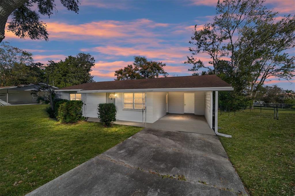 A single-story white house with a brown roof and an attached carport at dusk — 21529 SW HONEYSUCKLE STREET, DUNNELLON, FL