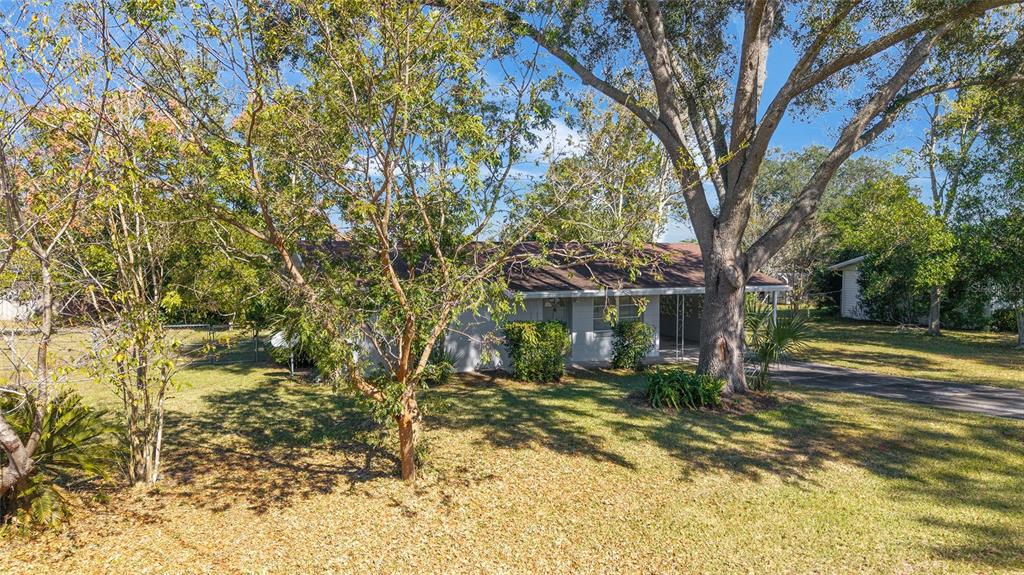 A single-story house with a carport sits on a grassy lot shaded by large trees — 21529 SW HONEYSUCKLE STREET, DUNNELLON, FL