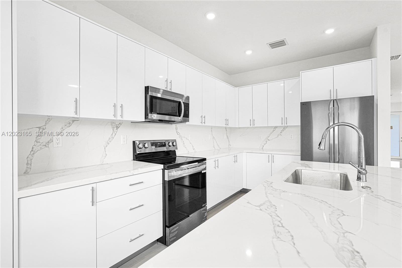 A modern kitchen features white flat-panel cabinets, marble-patterned countertops, and stainless steel appliances — 22555 SW 125 ave # 13A, Miami FL 33170, MIAMI, FL