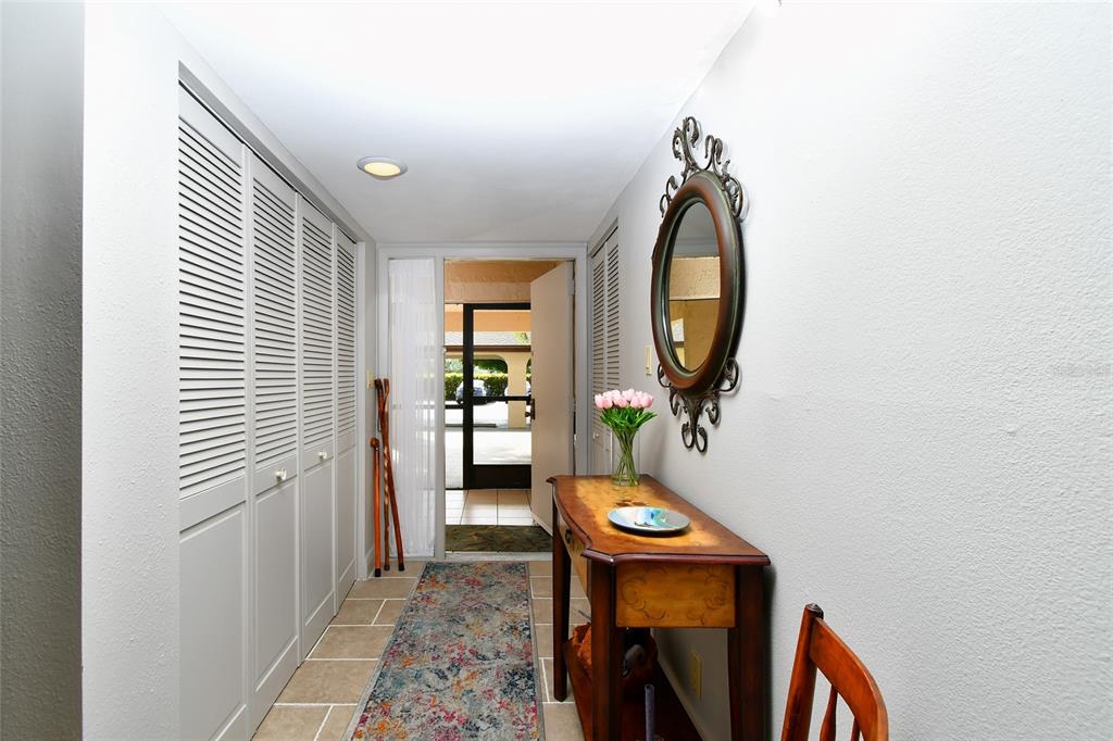 An entryway features a tiled floor, a wooden console table, a mirror, and louvered closet doors — 1610 N ISLAMORADA BOULEVARD UNIT 62A, PUNTA GORDA, FL