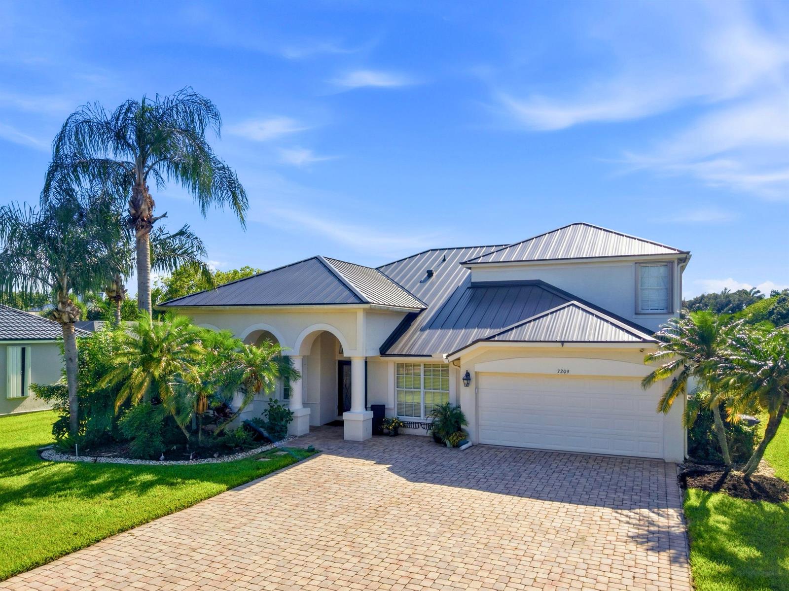 A two-story house with a metal roof, a paved driveway, and palm trees in the yard — 7209 Serrano Terrace, Delray Beach FL 33446, DELRAY BEACH, FL
