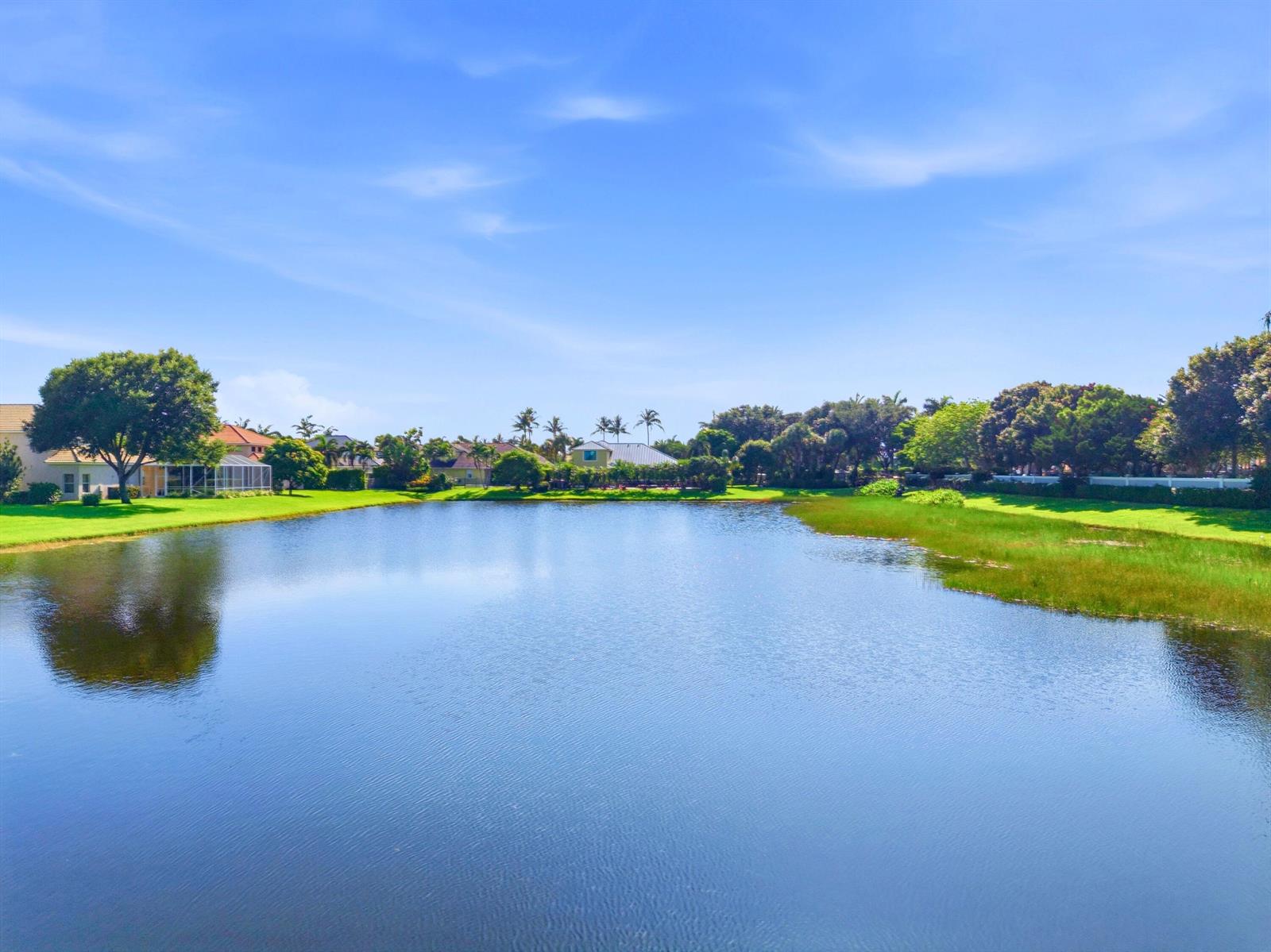 A calm lake surrounded by green lawns, trees, and residential houses under a blue sky — 7209 Serrano Terrace, Delray Beach FL 33446, DELRAY BEACH, FL