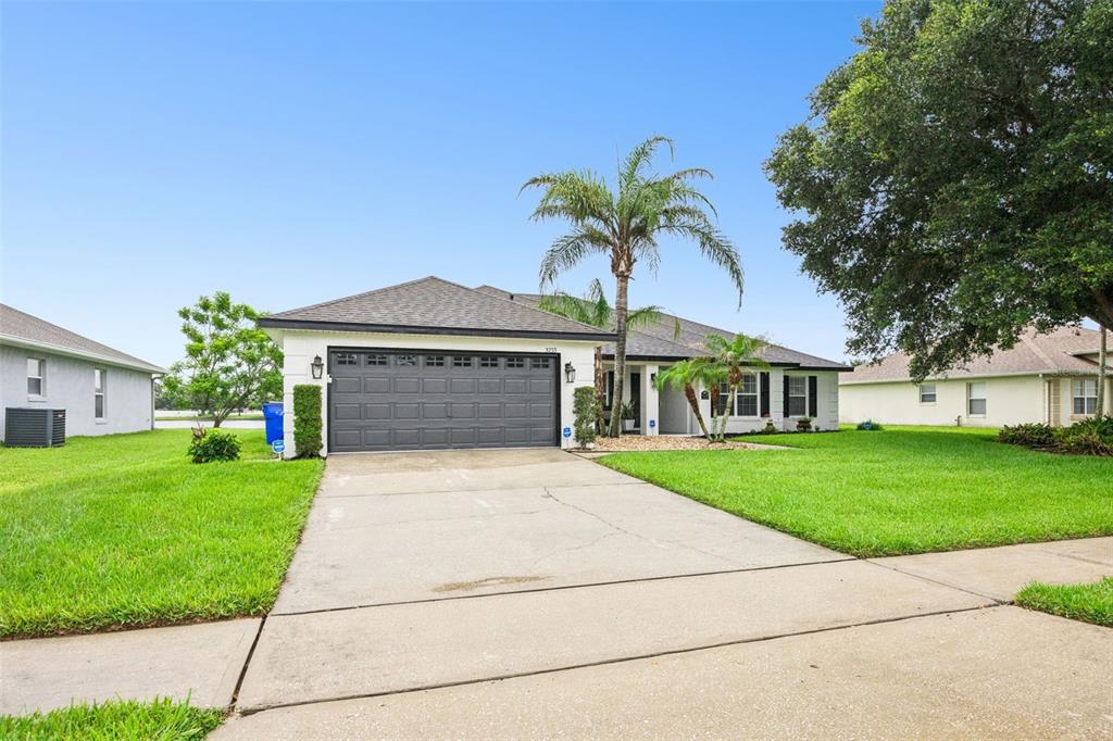 A single-story house with a gray garage door, white exterior, and a palm tree — 3233 LORIMAR LANE, ST CLOUD, FL