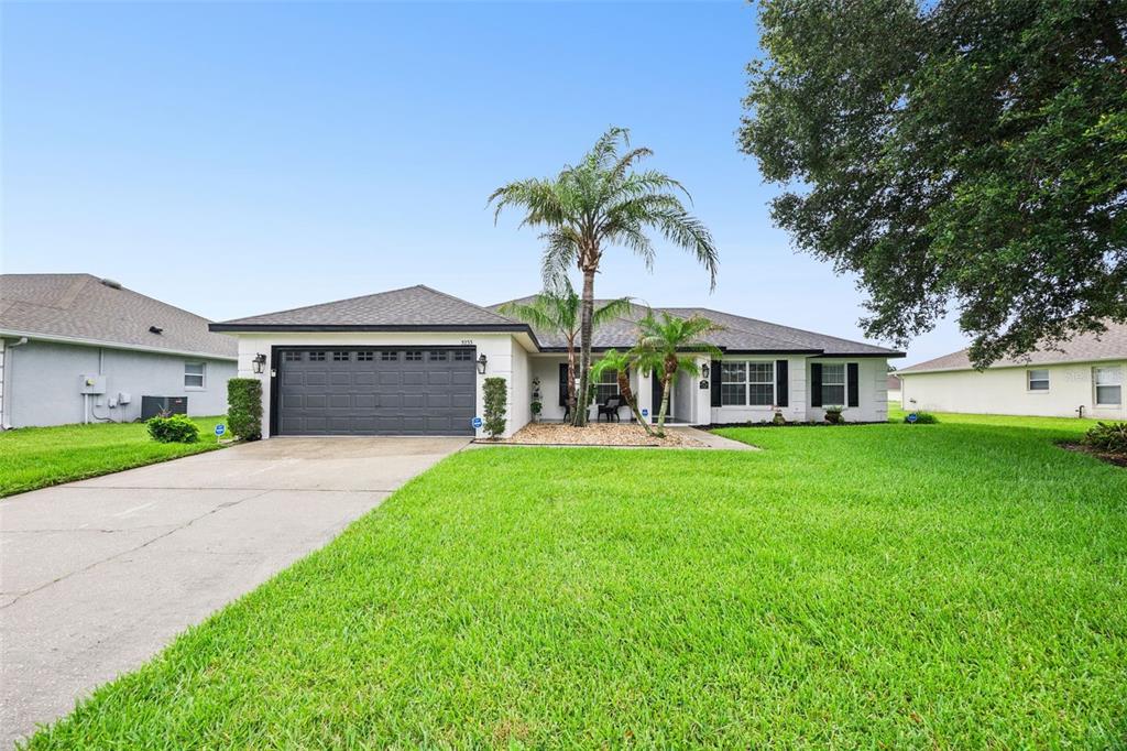 A single-story house with a dark garage door, white exterior, and a palm tree — 3233 LORIMAR LANE, ST CLOUD, FL