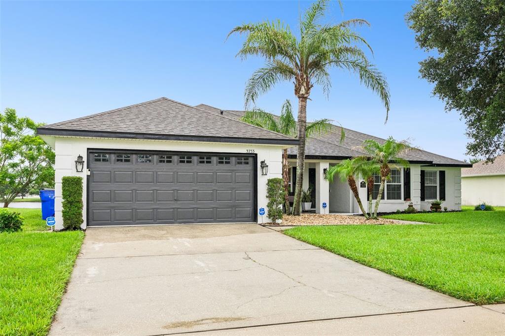 A single-story house with a white exterior, dark garage door, and a palm tree — 3233 LORIMAR LANE, ST CLOUD, FL