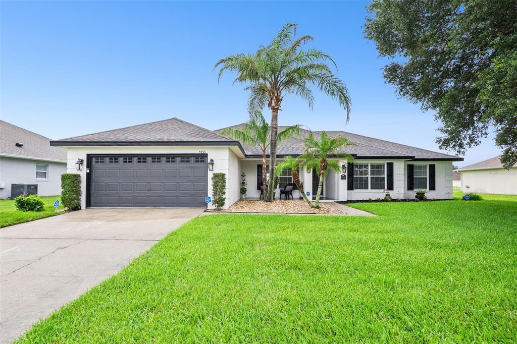 A single-story house with a white exterior, dark garage door, and a palm tree out front — 3233 LORIMAR LANE, ST CLOUD, FL
