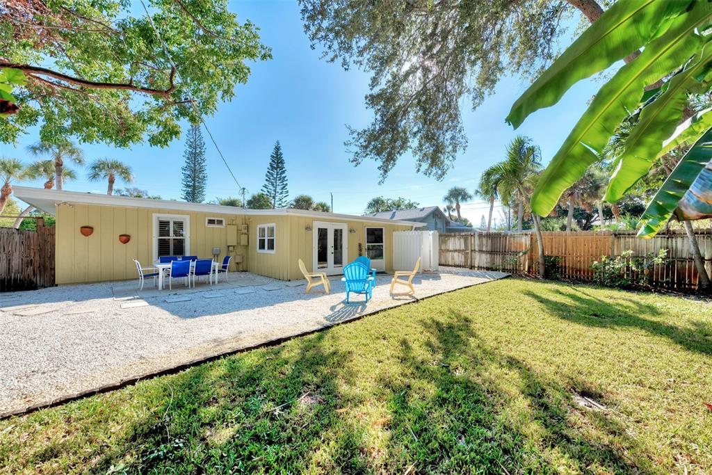 A yellow house with a gravel patio, outdoor seating, and a grassy backyard — 5216 CALLE DE COSTA RICA, SARASOTA, FL