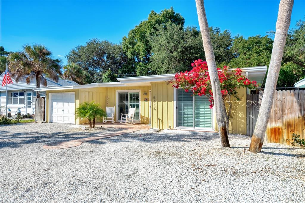 A yellow single-story house with a gravel yard, palm trees, and a red bougainvillea bush — 5216 CALLE DE COSTA RICA, SARASOTA, FL