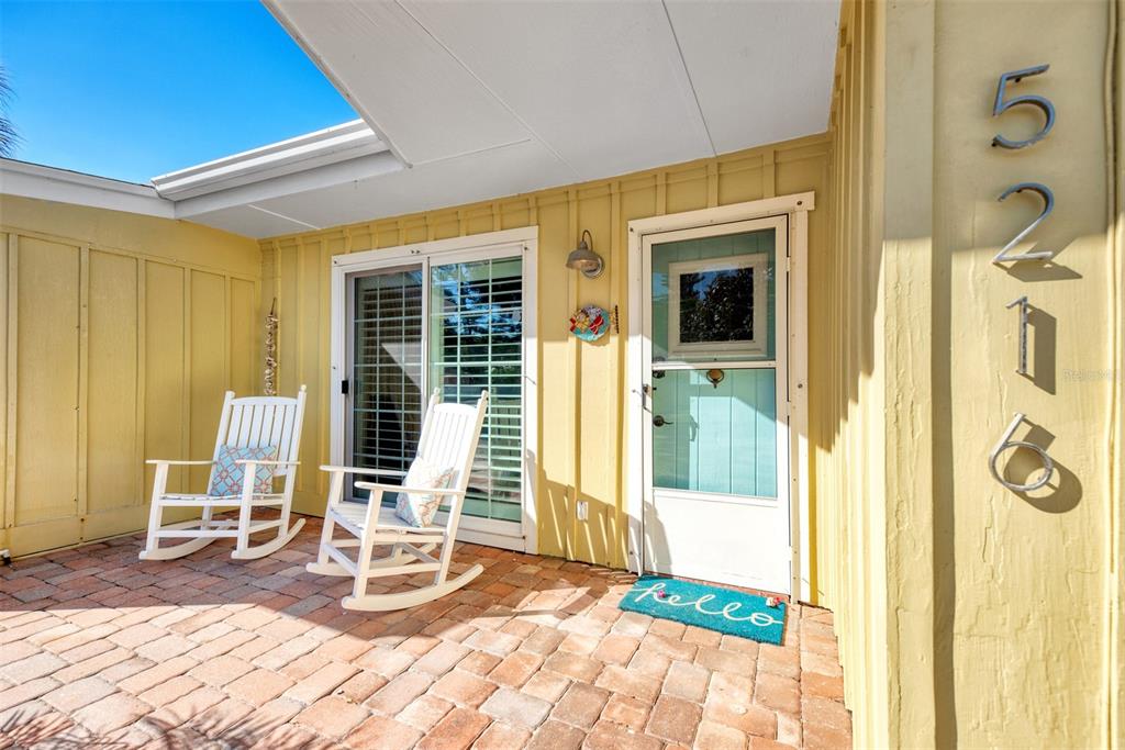 A brick patio features two white rocking chairs and a front door with a welcome mat — 5216 CALLE DE COSTA RICA, SARASOTA, FL