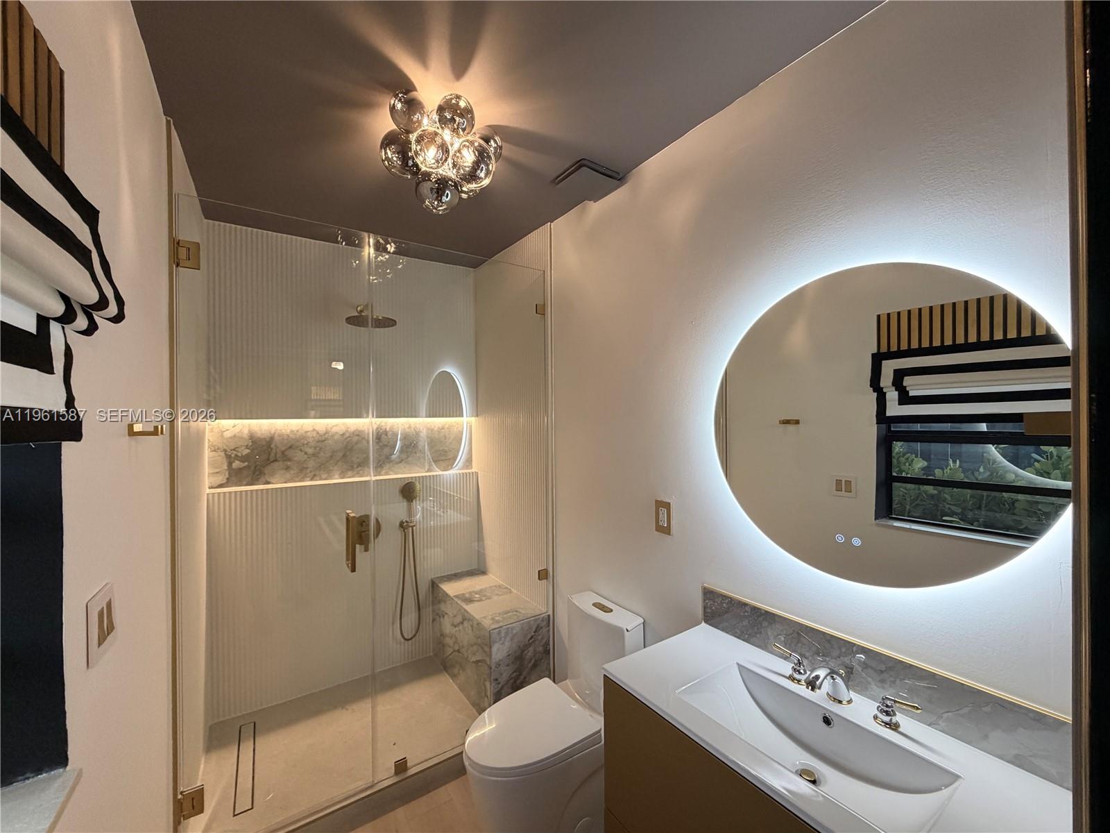 A modern bathroom features a glass-enclosed shower, a round backlit mirror, and gold fixtures — 920 SW 50th Ave, Plantation FL 33317, PLANTATION, FL