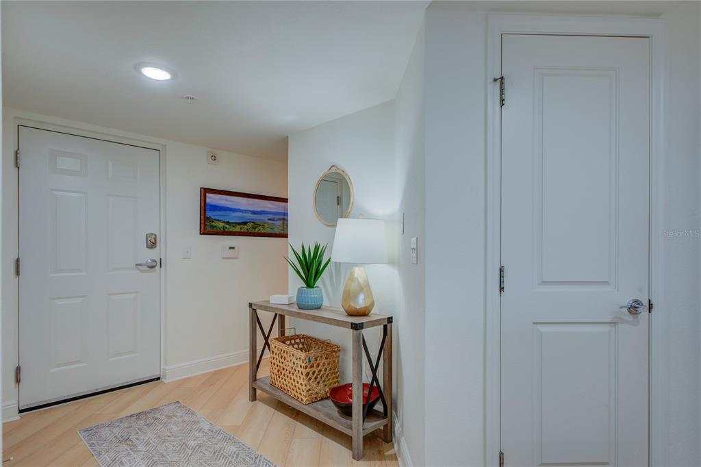 An entryway features a white door, a console table with decor, and light wood flooring — 5353 GULF BOULEVARD UNIT A502, ST PETE BEACH, FL