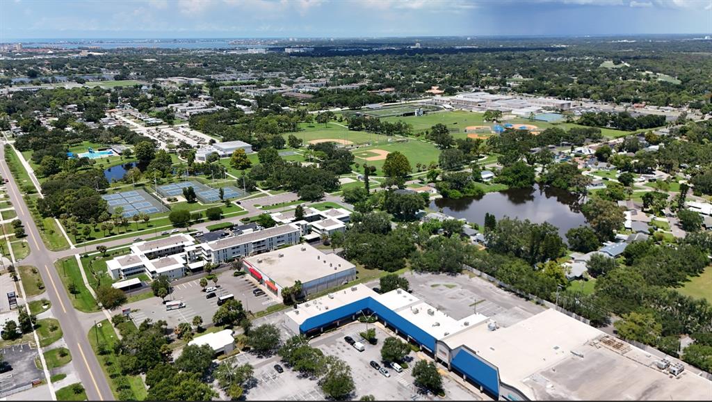 An aerial view shows a commercial building with a blue roof, parking lots, and nearby parks — 1050 62ND AVE SOUTH UNIT E-4, ST PETERSBURG, FL