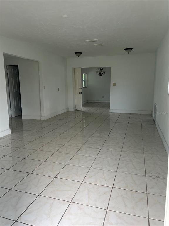 A room with white walls and light-colored tiled flooring leads into an adjacent dining area — 14405 DARING AVENUE, ORLANDO, FL